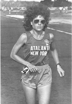 Marcy Schwam competing in the Edward Payson Weston six day race in 1980. Schwam is wearing a singlet with "Atalanta New York" in capital letters, shorts and sunglasses.