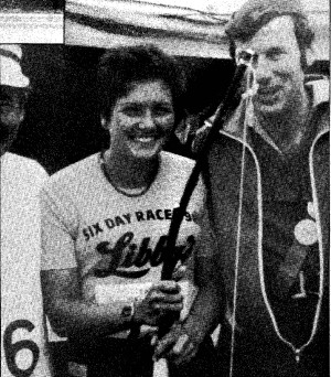A photograph showing ultrarunner Ros Paul smiling and holding a bow next to a man dressed as Robin Hood at the Nottingham Six Day Track Race in 1982