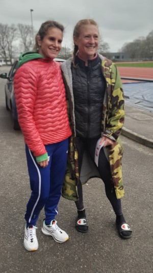 British ultrarunners Ali Young and Beccy Davis before the start of the Crawley 24 Hour Track race. They are both wearing warm clothes. Beccy is holding her race number in her left hand. They are both smiling.