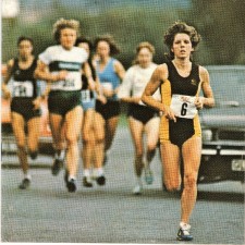 Julie Barleycorn leading the 1981 National 10 Mile Championship. She is wearing a black and yellow running best and matching pants and has the race number 6. Other runners are visible but out of focus in the background