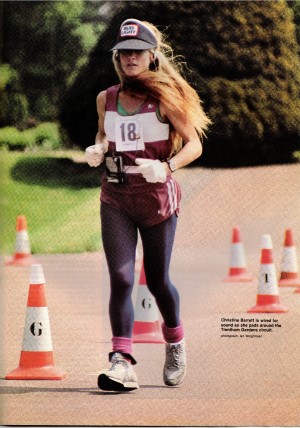 Christine Barrett ultrarunner competing in a six day race in 1984. She is wearing a maroon vest and shorts with dark tights underneath and pink legwarmers. She wears a dark visor with the words Bud Light and white gloves. She has a number 18 attached to her vest. She has a Walkman attached to a waist belt and headphones in her ears. Bottom right it says "Christine Barrett is wired for sound as she pads around the Trentham Gardens circuit".