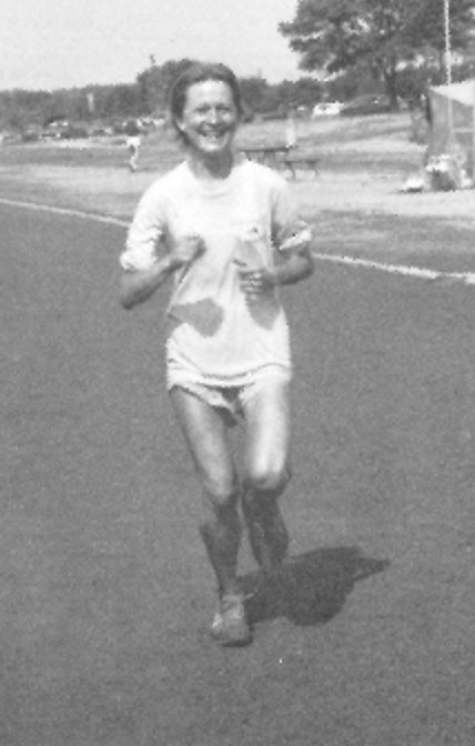Mary Hanudel ultrarunner competing in the Edward Payson Weston 6 Day Race in 1984. She is running and wearing a light coloured t-shirt and shorts. Her hair is short and she is smiling.
