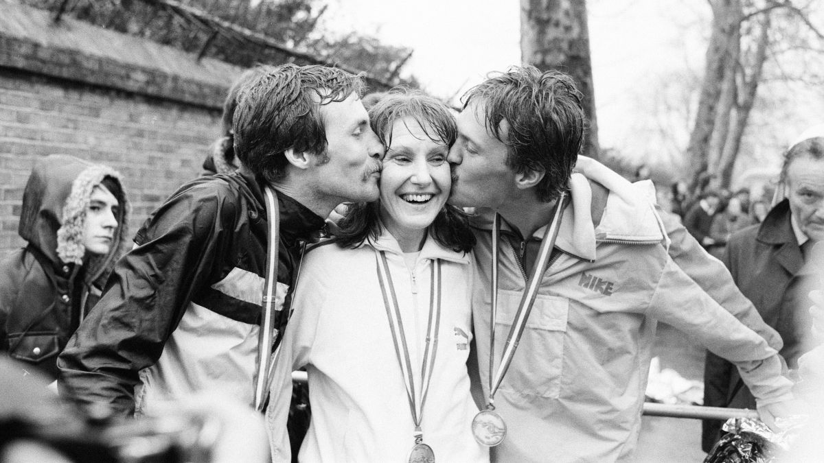 Joyce Smith winner of London Marathon 1981 is being kissed by Dick Beardsley and Inge Simonson the winners of the men's race. All three are wearing jackets and medals. Joyce Smith is smiling.