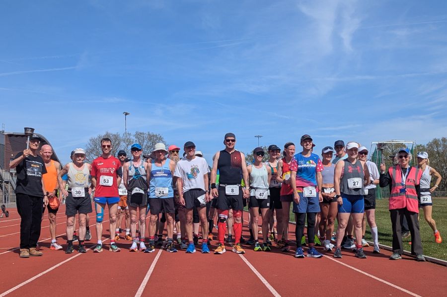 A group of runners lined up on an athletics track at the start of the Crawley 24-hour track race.