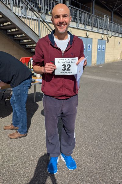 Ultrarunner Gordon Mead stands smiling and holding his race numbers.