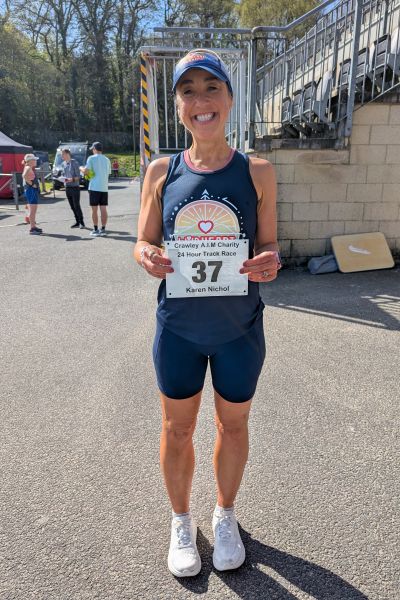Ultrarunner Karen Nicol stands smiling and holding her race number in front of her.
